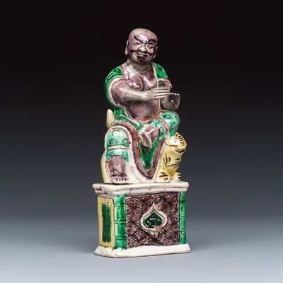 A Chinese famille verte sancai biscuit model of a seated Luohan on a tiger, Kangxi