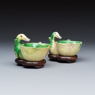 A pair of Chinese famille verte sancai biscuit duck-and-lotus-form water droppers on later wooden stands, Kangxi
