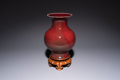 A Chinese copper-red-glazed vase on a wooden stand, 20th C.