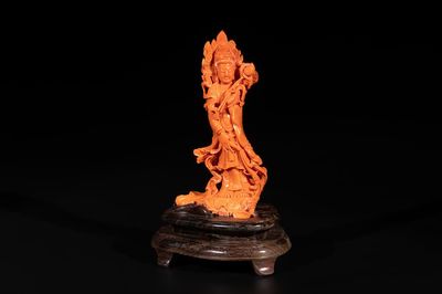 A Chinese red coral Guanyin holding a lotus on wooden stand, 19/20th C.