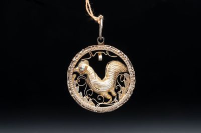 A gilt-brass 'Rooster' amulet with glass-inlaid eyes, 17th C. or later