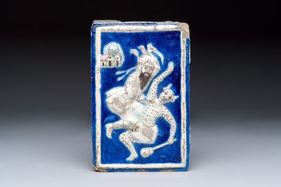 A Persian relief-moulded blue-ground tile depicting Fateh 'Ali Shah in the guise of Rustam slaying the White Div, Qajar, 19th C.