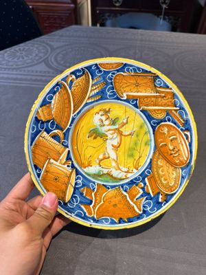 A polychrome Italian maiolica plate with a putto surrounded by trophies, Pesaro, 16th C. — photo 1