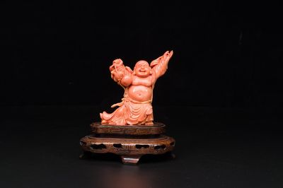 Een Chinese bloedkoralen figuur van een lachende Boeddha op houten sokkel, 19/20e eeuw