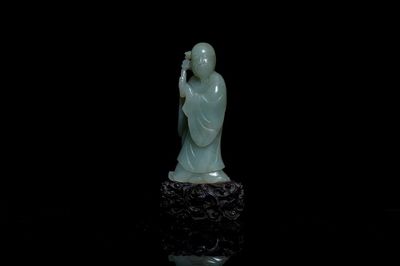 Een Chinese figuur van een onsterfelijke in celadon jade op houten sokkel, Qing