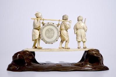 A large Japanese ivory okimono of boys playing a drum on a carved wooden base, Meiji, late 19th C., signed