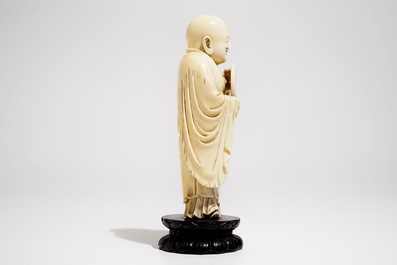 A Chinese carved ivory figure of Buddha holding a fan, on lotus-shaped base, 19th C.