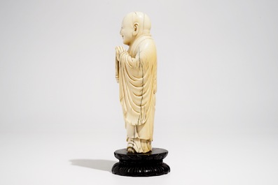 A Chinese carved ivory figure of Buddha holding a fan, on lotus-shaped base, 19th C.