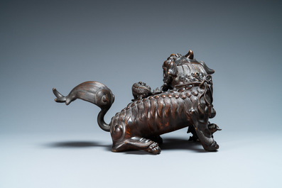 A Chinese bronze model of a Buddhist lion on a finely carved wooden stand, 18th C.