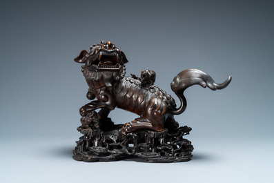 A Chinese bronze model of a Buddhist lion on a finely carved wooden stand, 18th C.