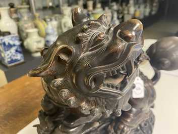 A Chinese bronze model of a Buddhist lion on a finely carved wooden stand, 18th C.