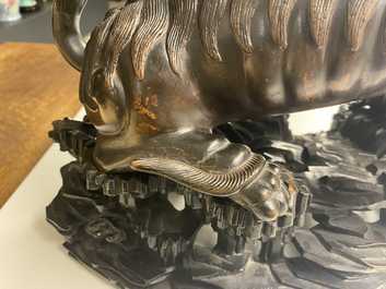 A Chinese bronze model of a Buddhist lion on a finely carved wooden stand, 18th C.