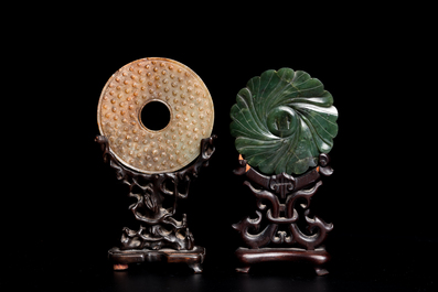 A Chinese celadon and russet jade 'bi' disc and a spinach green flower-shaped pendant on wooden stands, Ming and Qing