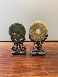 A Chinese celadon and russet jade 'bi' disc and a spinach green flower-shaped pendant on wooden stands, Ming and Qing