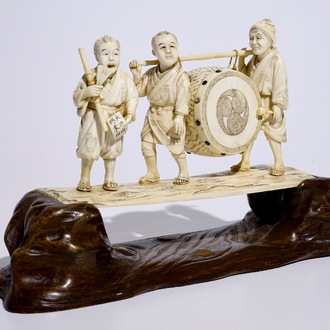 A large Japanese ivory okimono of boys playing a drum on a carved wooden base, Meiji, late 19th C., signed