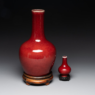 Two Chinese monochrome copper-red-glazed bottle vases on wooden stands, 19th C.