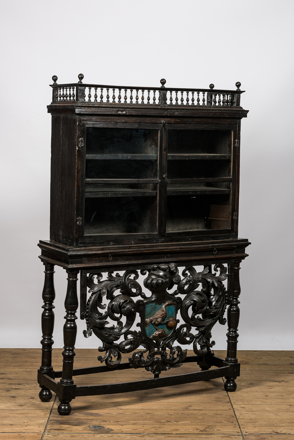 A Spanish ebonised wooden display cabinet on richly carved armorial stand, 19th C.