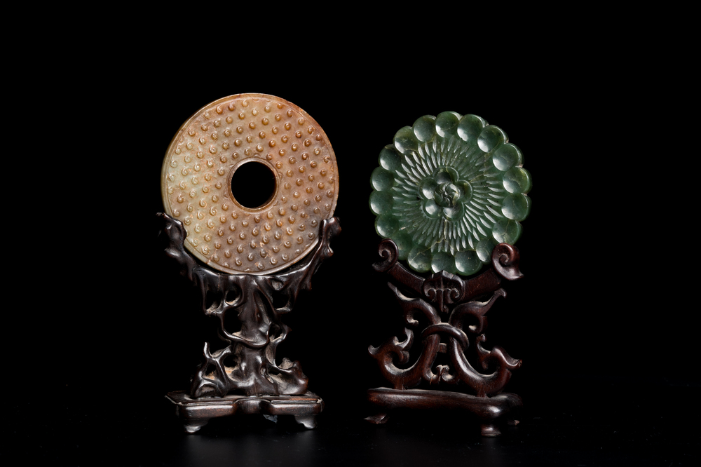 A Chinese celadon and russet jade 'bi' disc and a spinach green flower-shaped pendant on wooden stands, Ming and Qing