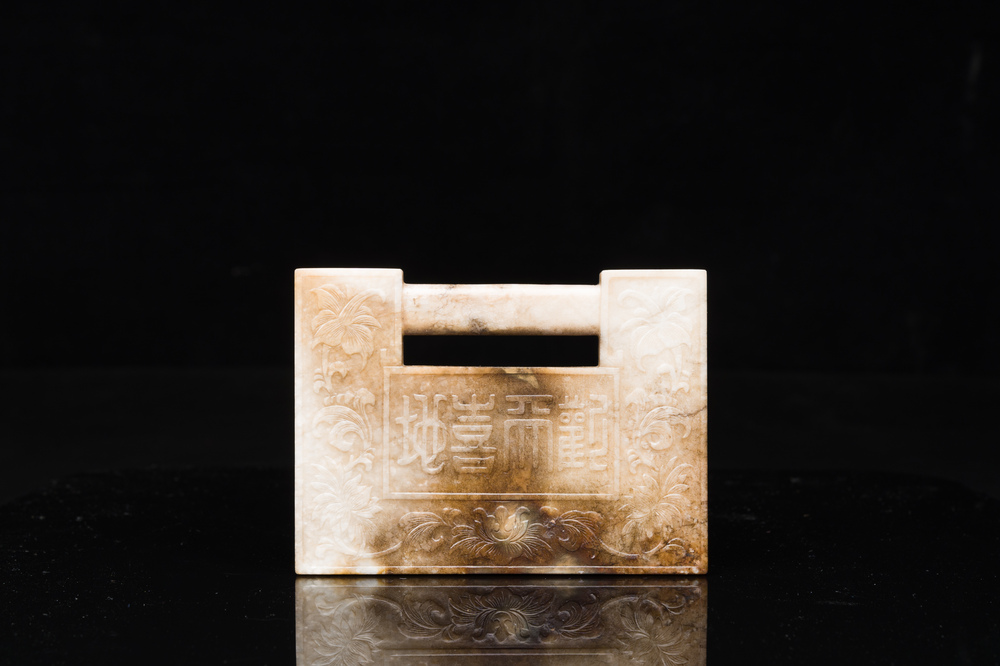 A Chinese white and russet jade lock-shaped plaque with inscription 'Huan Tian Xi Di 歡天喜地', Qing
