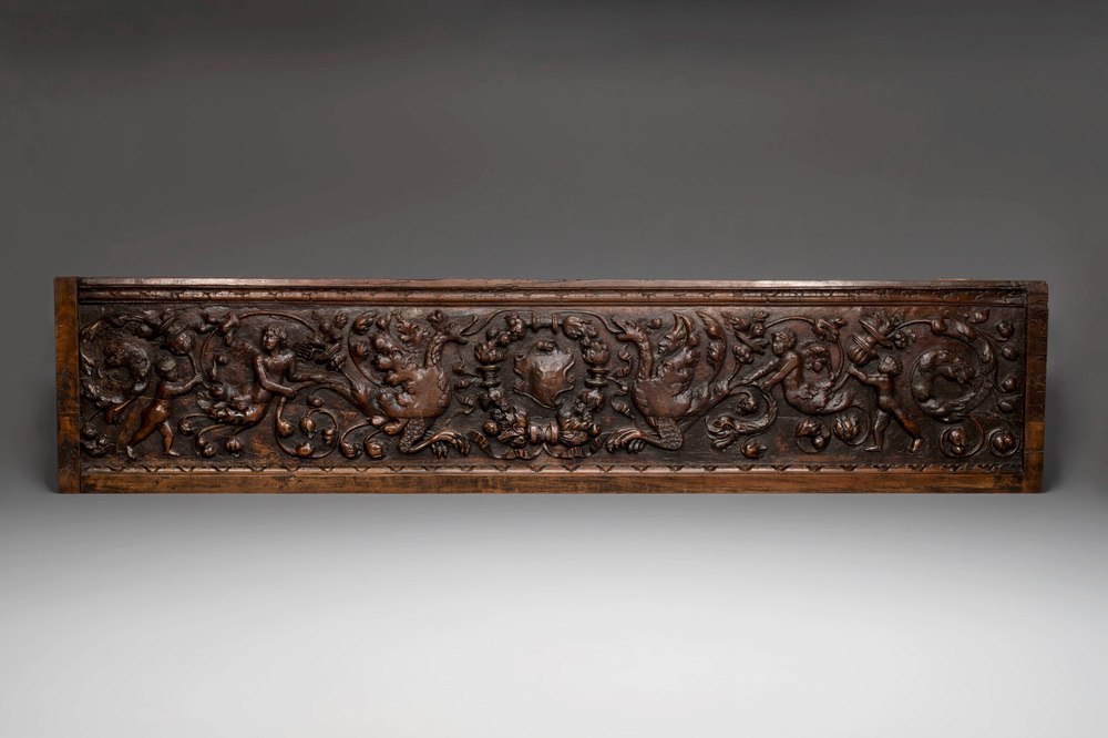 A sculptured walnut panel with putti, allegorical characters and human-headed dragons around an ecusson, presumably France, 16th C.